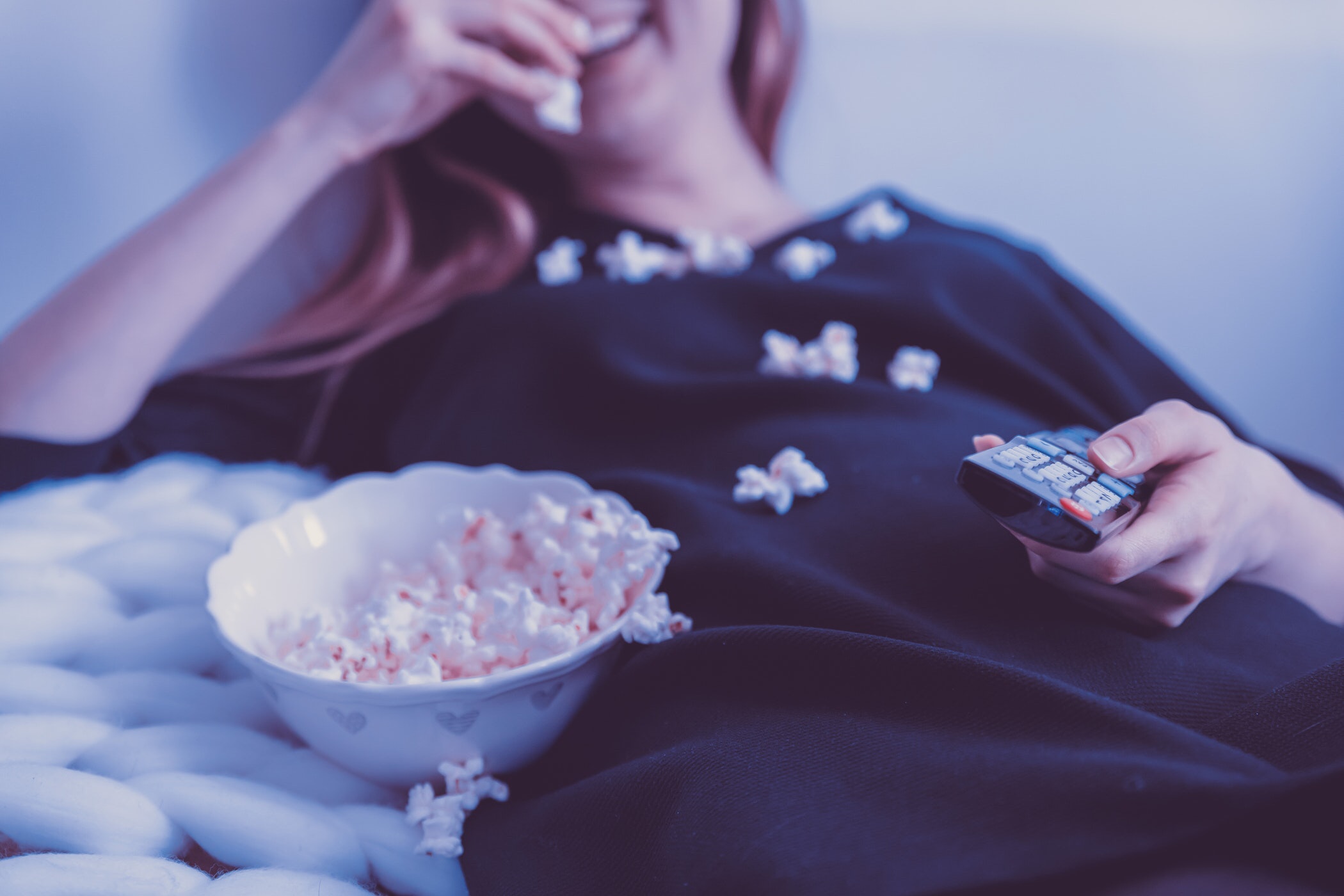 Woman eating popcorn with TV remote in bed