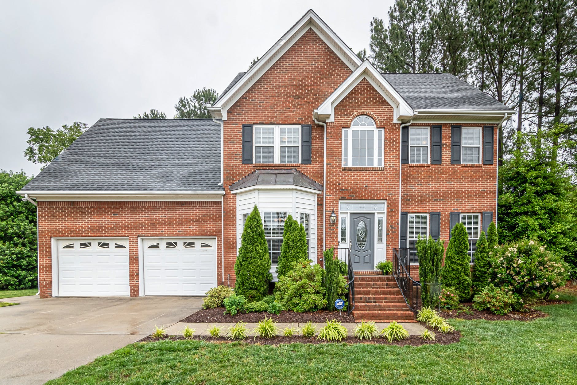 photo of red brick 2 story home with 2 car attached garage and stairs leading to entrance