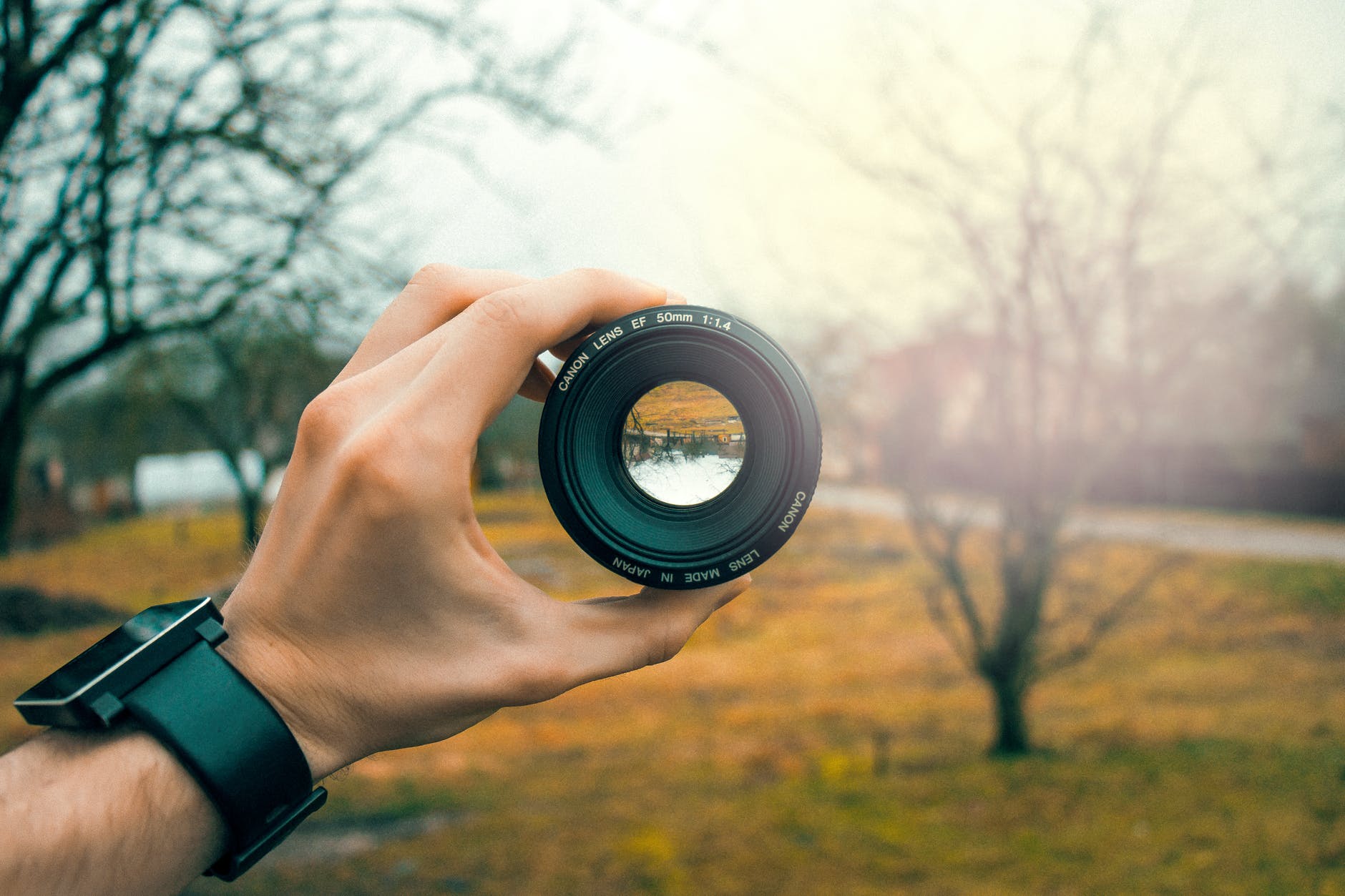 photo of male hand holding a camera lens with scenic background